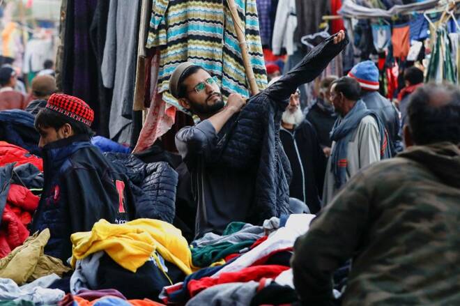 Man checks the size of a jacket at a stall selling secondhand clothes, at the Landa Bazar in Karachi