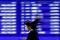 A passerby walks past an electric monitor displaying recent movements of various stock prices outside a bank in Tokyo