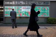 A woman walks past a man examining an electronic board showing Japan's Nikkei average and stock quotations in Tokyo
