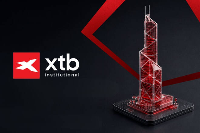 XTB Institutional logo alongside an illuminated transparent miniature model of the Bank of China Tower on a dark background with red geometric accents.