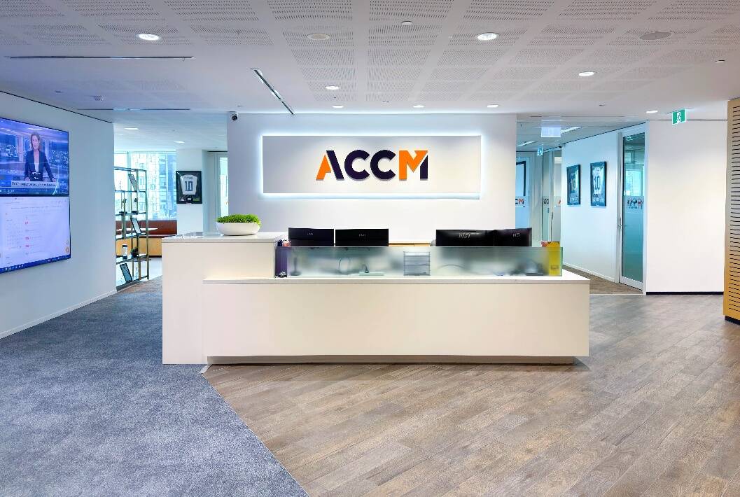 Modern office reception area featuring a white front desk with computer monitors and an illuminated 
