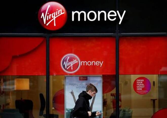A man checks his phone as he walks past a branch of Virgin Money in Manchester