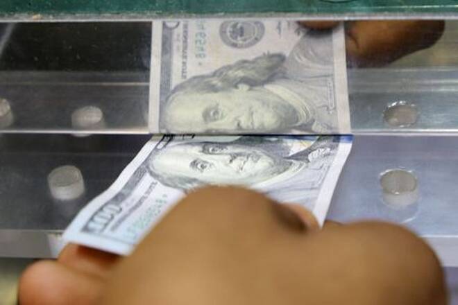 Man inserts a U.S. dollar banknote into the window of a local currency exchange in Aden