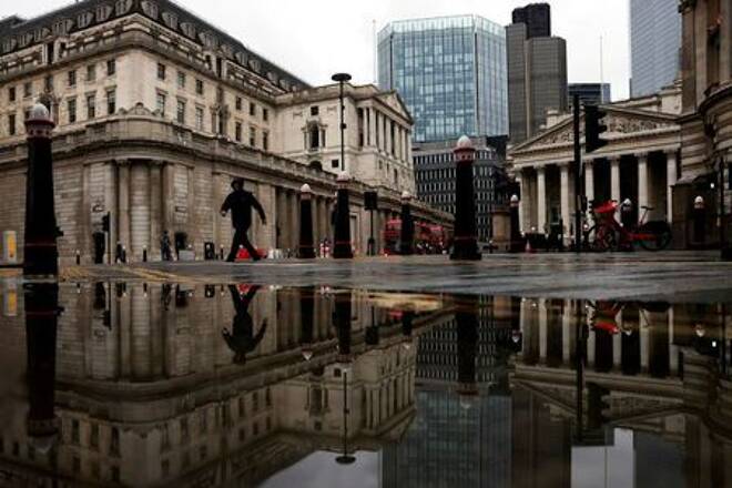 FILE PHOTO: The Bank of England and Royal Exchange are reflected in a puddle as a pedestrian walks past in London