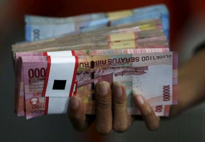An employee of a money changer holds a stack of Indonesia rupiah notes before giving it to a customer in Jakarta