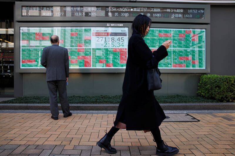 FOTO DE ARCHIVO. Una mujer camina cerca de un hombre que examina un tablero electrónico que muestra el promedio Nikkei de Japón y las cotizaciones bursátiles fuera de una casa de bolsa, en Tokio, Japón