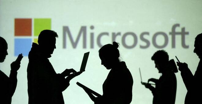 Imagen de archivo ilustrativa de siluetas de usuarios de computadores portátiles y dispositivos móviles junto a una proyección del logotipo de Microsoft en una pantalla