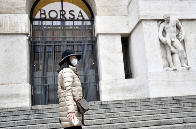 Una donna con una maschera davanti l'ingresso della Borsa di Milano